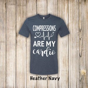 May include: A heather navy blue t-shirt with the text "COMPRESSIONS ARE MY cardio" in white. A white heart with a stethoscope and a heartbeat line are above the text.