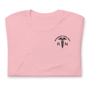 Folded light pink ICU nurse shirt with black Intensive Care Unit RN chest graphic.