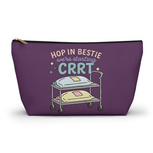 May include: A purple zippered pouch with the text "HOP IN BESTIE we're starting CRRT" in pink and blue. The design includes a cartoon illustration of a medical cart with two pillows. The pouch has a gold zipper.