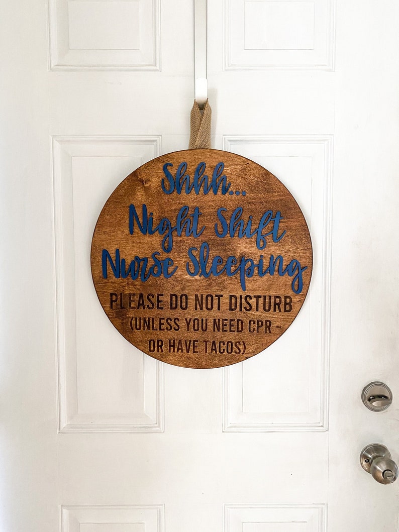 May include: A round wooden sign with the text "Shhh... Night Shift Nurse Sleeping. Please do not disturb (unless you need CPR or have tacos)" in blue lettering.