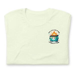 Puede incluir: Una camiseta verde claro con un gr&aacute;fico de un contenedor de basura verde en llamas con una cara blanca y el texto "This little light of mine I'm gonna let it shine".