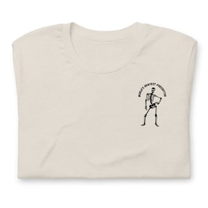 May include: A beige t-shirt with a black skeleton graphic and the text "World's Okayest Preceptor" printed on the front.