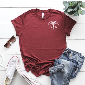 Puede incluir: Camiseta color burdeos con un gr&aacute;fico blanco de un caduceo m&eacute;dico y el texto "Intensive Care Unit RN".
