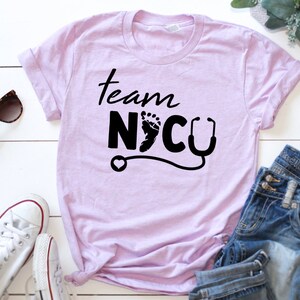 May include: A light purple t-shirt with the text "Team NICU" in black lettering. The text includes a small footprint and a stethoscope.