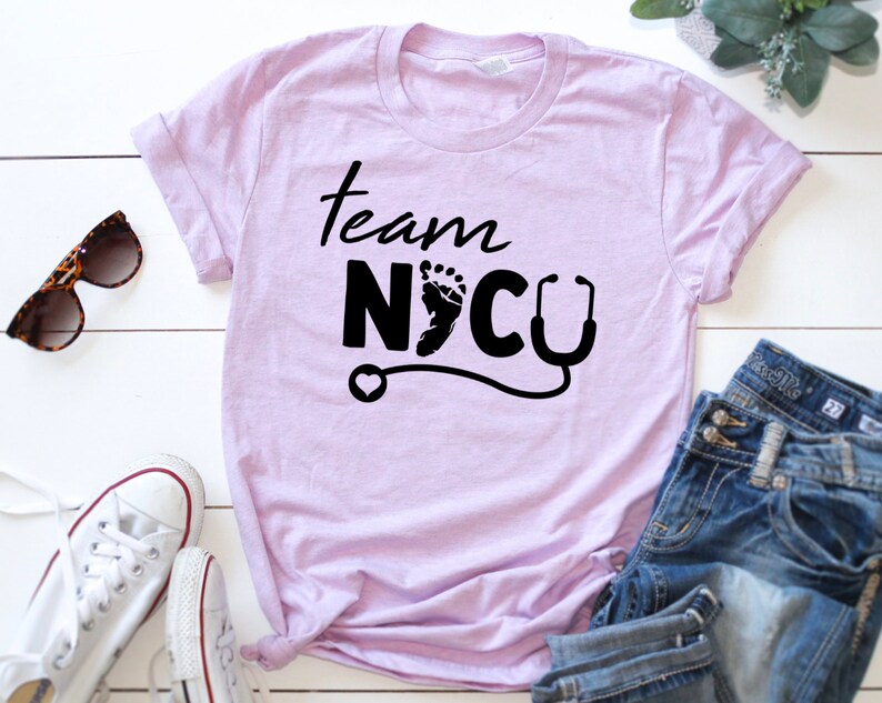 May include: A light purple t-shirt with the text "Team NICU" in black lettering. The text includes a small footprint and a stethoscope.