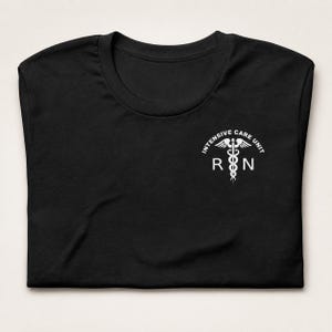 Folded black ICU nurse shirt with white Intensive Care Unit RN left-chest design.