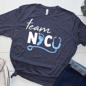 May include: A navy blue t-shirt with the text "Team NICU" in white lettering. A blue baby footprint and a stethoscope are included in the design.