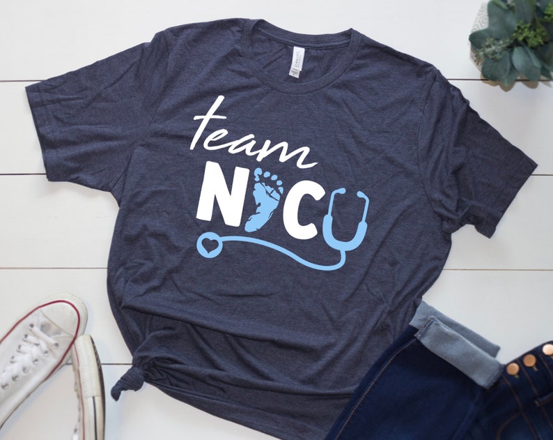 May include: A navy blue t-shirt with the text "Team NICU" in white lettering. A blue baby footprint and a stethoscope are included in the design.