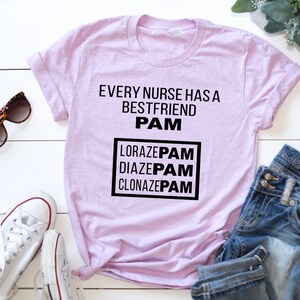 May include: A light purple t-shirt with the text "Every nurse has a best friend PAM" and a box with the text "LORAZEPAM DIAZEPAM CLONAZEPAM" in black.