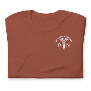 Folded rust-colored ICU nurse shirt with white critical care RN chest graphic.