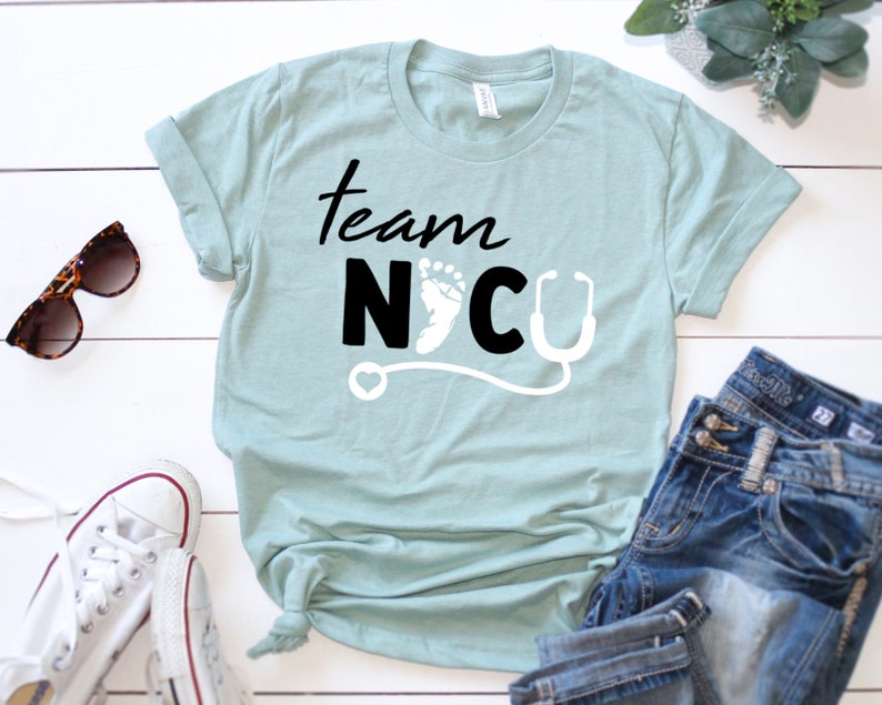 May include: A light blue t-shirt with the text "Team NICU" in black lettering. The text is accompanied by a white stethoscope and a white footprint.