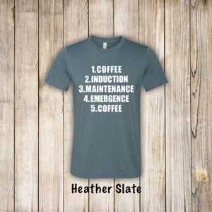 May include: A heather slate t-shirt with white text that reads "1. Coffee 2. Induction 3. Maintenance 4. Emergence 5. Coffee".