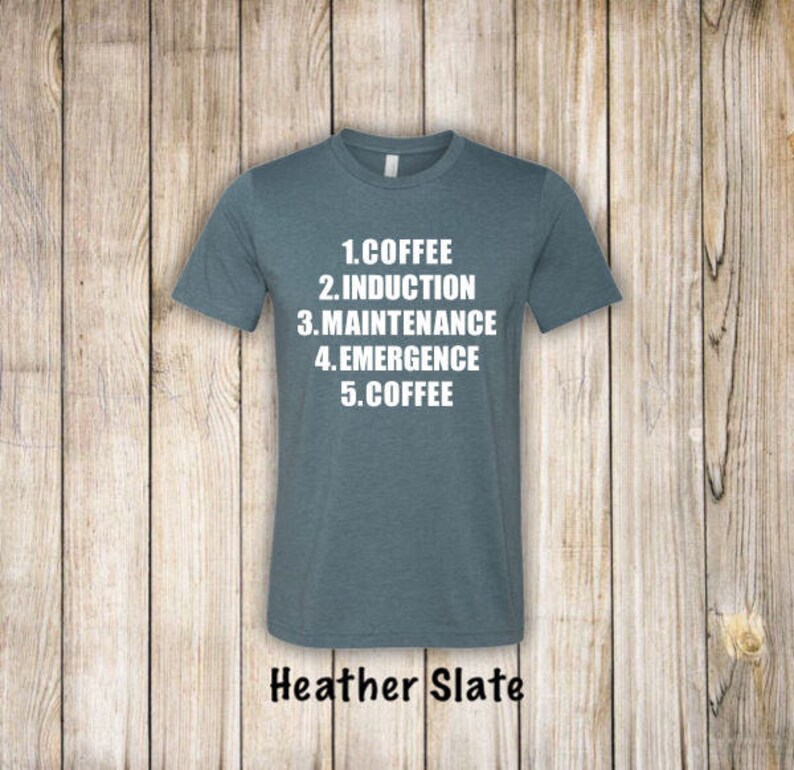 May include: A heather slate t-shirt with white text that reads "1. Coffee 2. Induction 3. Maintenance 4. Emergence 5. Coffee".