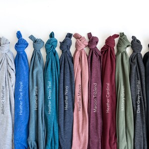 May include: A row of folded t-shirts in various colors, including white, gray, blue, teal, navy, pink, maroon, red, green, black, and dark gray. The t-shirts are arranged from left to right in order of color.
