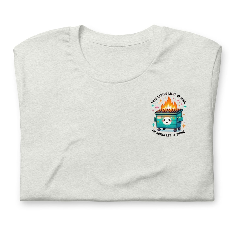 Puede incluir: Una camiseta gris claro con un gr&aacute;fico de un contenedor de basura verde en llamas con el texto "This little light of mine, I'm gonna let it shine."