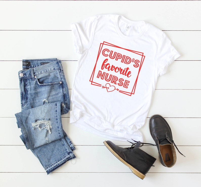 May include: White t-shirt with red text that says "Cupid's Favorite Nurse" with a red heart and arrow below the text.