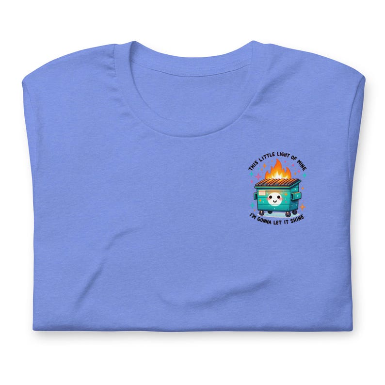 Puede incluir: Una camiseta azul claro con un gr&aacute;fico de un contenedor de basura verde en llamas con una cara sonriente y el texto "This little light of mine, I'm gonna let it shine."