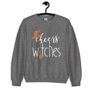 Op de afbeelding: Een donkergrijs gem&ecirc;leerd sweatshirt met ronde hals en de witte tekst "cheers witches" op de voorzijde. Het ontwerp bevat een oranje heksenhoed boven het woord cheers en een oranje bezemsteel die de letter i in witches vervangt.