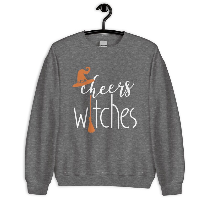 Op de afbeelding: Een donkergrijs gem&ecirc;leerd sweatshirt met ronde hals en de witte tekst "cheers witches" op de voorzijde. Het ontwerp bevat een oranje heksenhoed boven het woord cheers en een oranje bezemsteel die de letter i in witches vervangt.