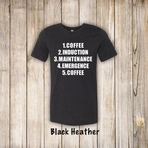May include: A black heather t-shirt with white text that reads "1. Coffee 2. Induction 3. Maintenance 4. Emergence 5. Coffee".