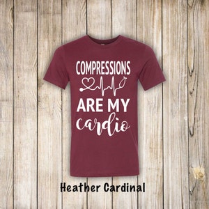 May include: A maroon t-shirt with white text that reads "COMPRESSIONS ARE MY cardio" with a stethoscope and a heart beat graphic.