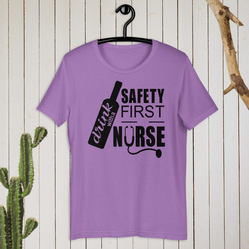 K&ouml;nnte beinhalten: Lilafarbenes T-Shirt mit einer schwarzen Grafik einer Weinflasche und dem Text "drink with a nurse" und "safety first".