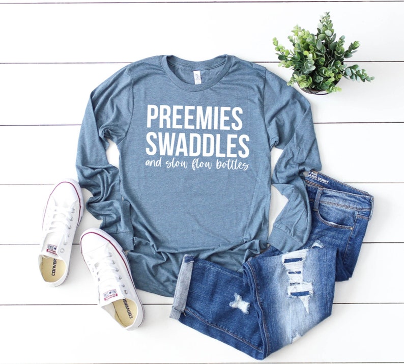 May include: A teal blue long-sleeved t-shirt with the text "Preemies Swaddles and slow flow bottles" in white.
