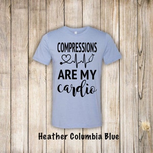 May include: Light blue t-shirt with black text that reads "COMPRESSIONS ARE MY cardio" with a heart and EKG graphic.