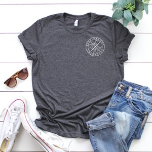 May include: A dark heather grey t-shirt with a white graphic of a cross with a compass and the words "Aspirational" and "Habitual" around it.