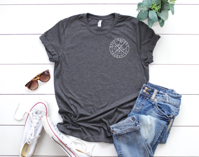 May include: A dark heather grey t-shirt with a white graphic of a cross with a compass and the words "Aspirational" and "Habitual" around it.