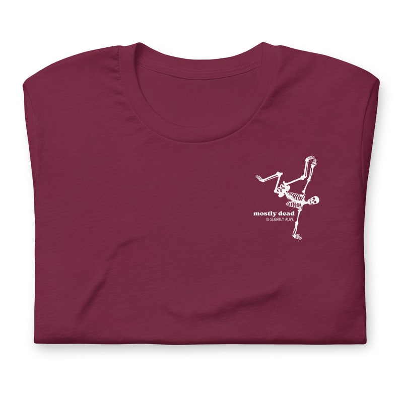 Puede incluir: Camiseta color burdeos con un gr&aacute;fico de esqueleto blanco y el texto "mostly dead is slightly alive".