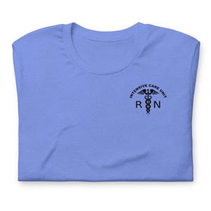 Folded periwinkle blue ICU nurse shirt with black ICU RN left-chest design.