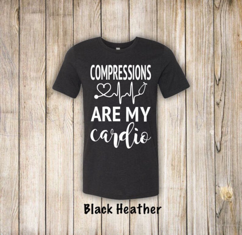 May include: Black heather grey t-shirt with white text that reads "COMPRESSIONS ARE MY cardio" with a heart and EKG line graphic.