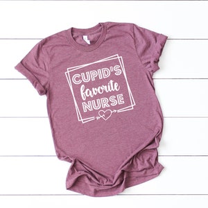 May include: A maroon t-shirt with the text "CUPID'S favorite NURSE" in white lettering inside a white box with a heart and arrow.