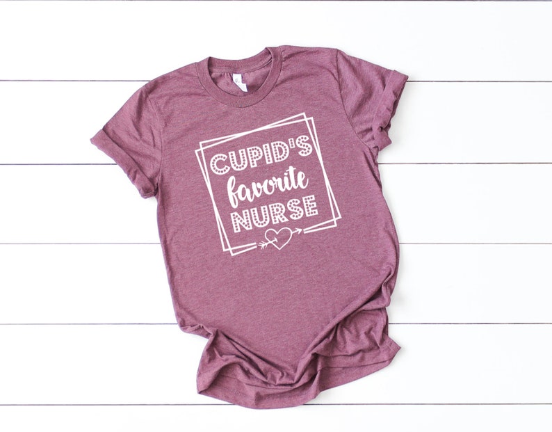 May include: A maroon t-shirt with the text "CUPID'S favorite NURSE" in white lettering inside a white box with a heart and arrow.