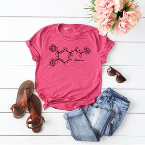 May include: A pink t-shirt with a black graphic of a dopamine molecule with roses. The text "dopamine" is written below the molecule.