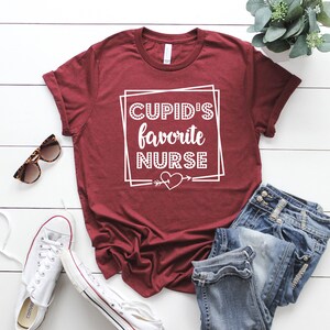 May include: A maroon t-shirt with white text that reads "CUPID'S favorite NURSE" with a heart and arrow graphic.