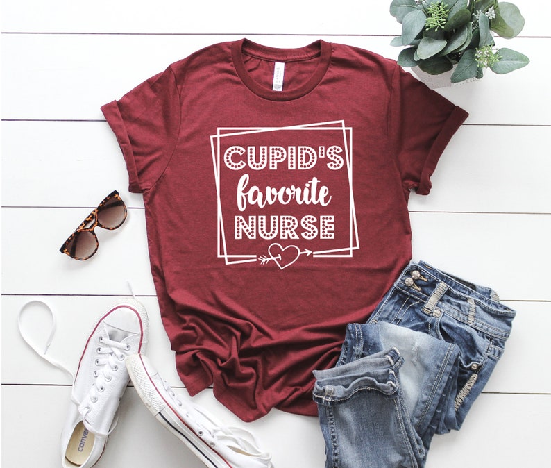 May include: A maroon t-shirt with white text that reads "CUPID'S favorite NURSE" with a heart and arrow graphic.