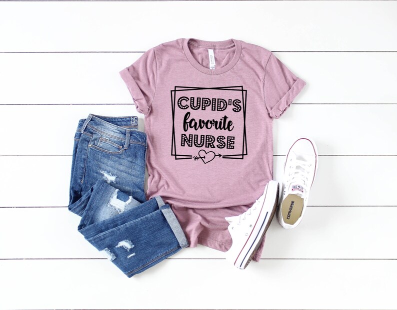 May include: A mauve t-shirt with the text "CUPID'S favorite NURSE" in a black square frame with a heart and arrow.