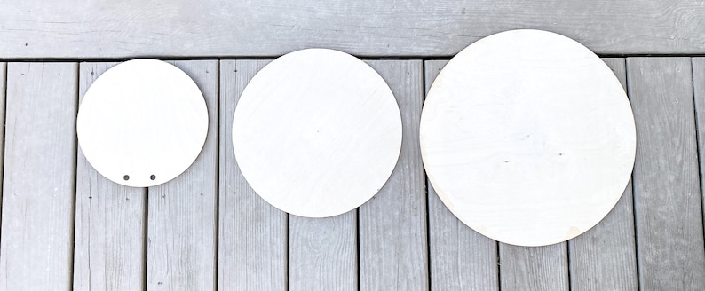 Peut inclure: Trois disques ronds en bois blanc de tailles diff&eacute;rentes. Les disques sont dispos&eacute;s du plus petit au plus grand, de gauche &agrave; droite. Le plus petit disque a deux petits trous au centre.