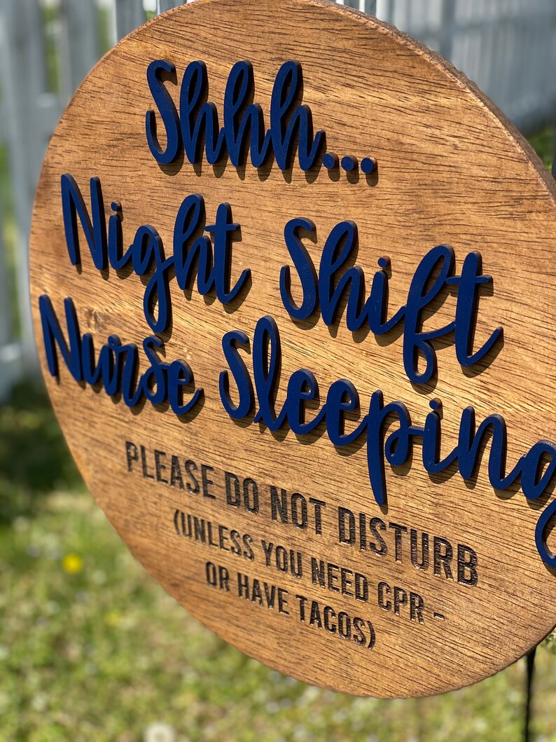 May include: A round wooden sign with the text "Shhh... Night Shift Nurse Sleeping Please Do Not Disturb (Unless You Need CPR - Or Have Tacos)" in blue lettering.