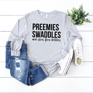 May include: Gray long-sleeve shirt with the text "Preemies Swaddles and slow flow bottles" printed in black.