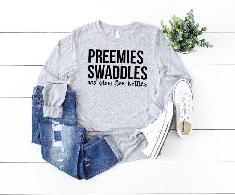 May include: Gray long-sleeve shirt with the text "Preemies Swaddles and slow flow bottles" printed in black.