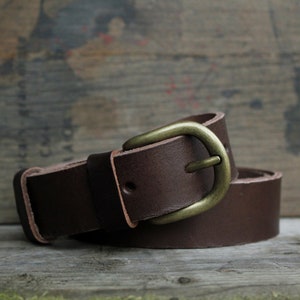Peut inclure: Une ceinture en cuir marron avec une boucle en laiton. La ceinture est pliée en deux et la boucle est visible.
