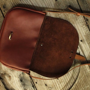 Może przedstawiać: Brązowa sk&oacute;rzana torba na ramię z klapką i długim, regulowanym paskiem. Torba ma podszewkę ze sk&oacute;ry zamszowej i klamrę mosiężną.