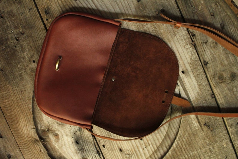 Może przedstawiać: Brązowa sk&oacute;rzana torba na ramię z klapką i długim, regulowanym paskiem. Torba ma podszewkę ze sk&oacute;ry zamszowej i klamrę mosiężną.