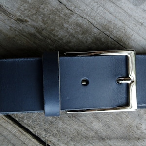 May include: A dark blue leather belt with a silver buckle. The belt is made of thick, durable leather and has a simple, classic design.