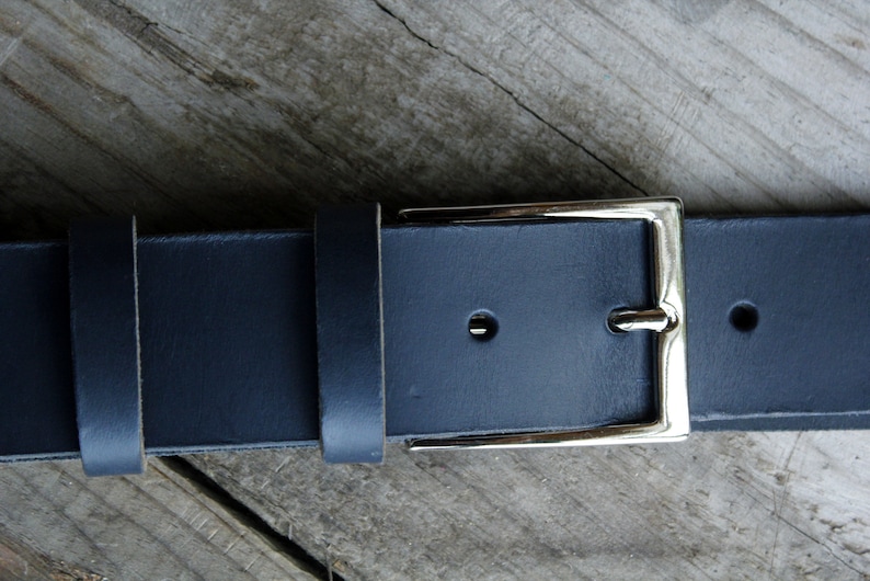 May include: A dark blue leather belt with a silver buckle. The belt is made of thick, durable leather and has a simple, classic design.