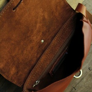 Może przedstawiać: Brązowa sk&oacute;rzana torba na ramię z kieszenią zapinaną na zamek błyskawiczny i klapką. Torba ma długi pasek i metalowy pierścień.