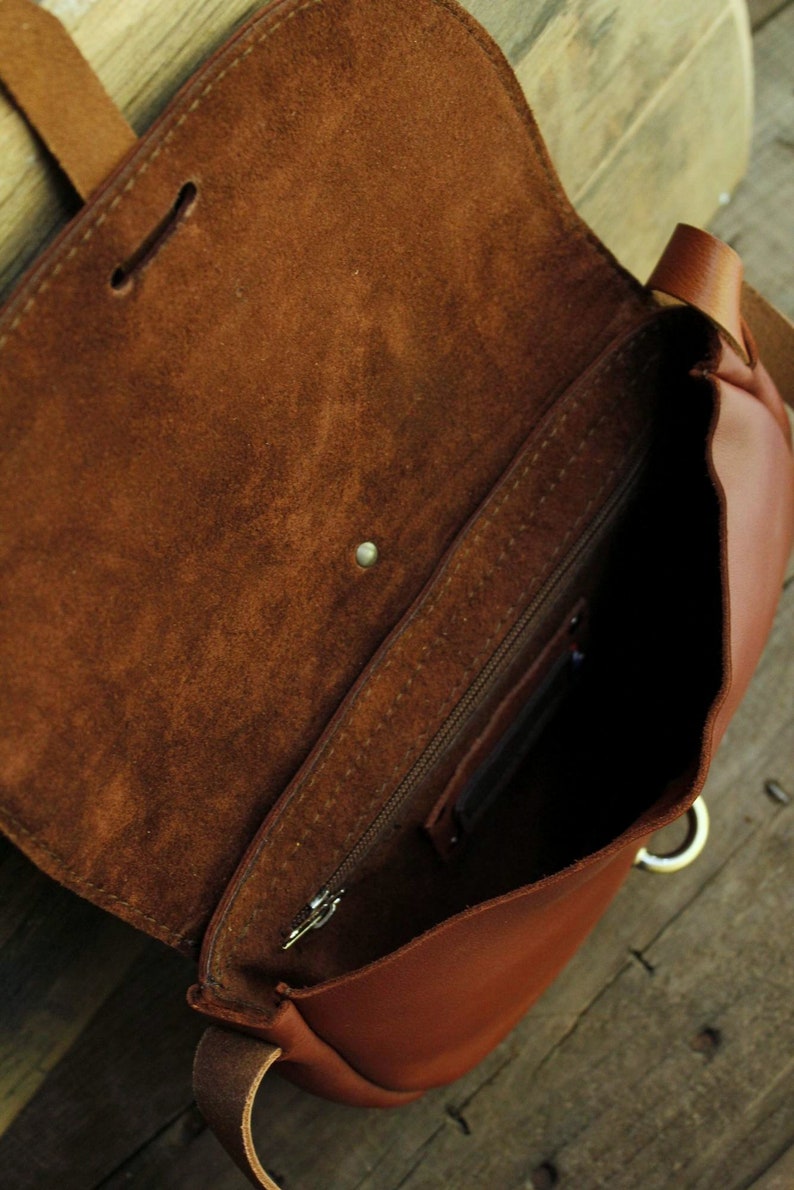 Może przedstawiać: Brązowa sk&oacute;rzana torba na ramię z kieszenią zapinaną na zamek błyskawiczny i klapką. Torba ma długi pasek i metalowy pierścień.